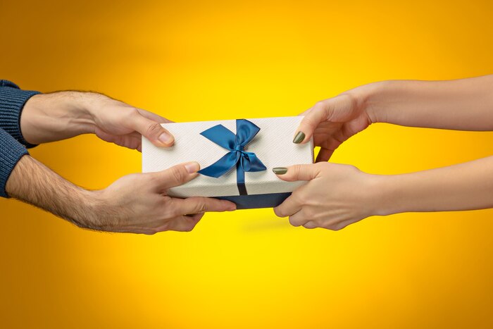 Closeup picture of man and woman\'s hands with gift box on yellow background