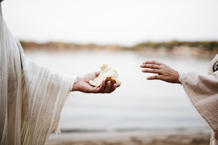 Closeup shot of a person wearing a biblical robe giving bread to another person