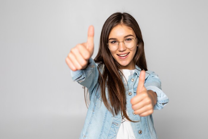 Young woman with thumbs up isolated over a white wall