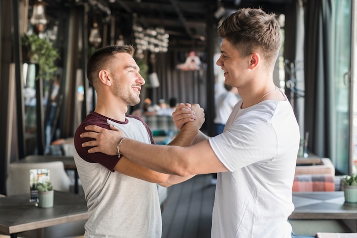 Two happy young male friends shaking hands in restaurant