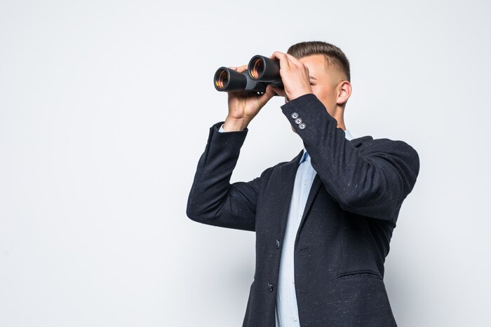 Businessman is looking through a pair of binoculars isolated on white wall