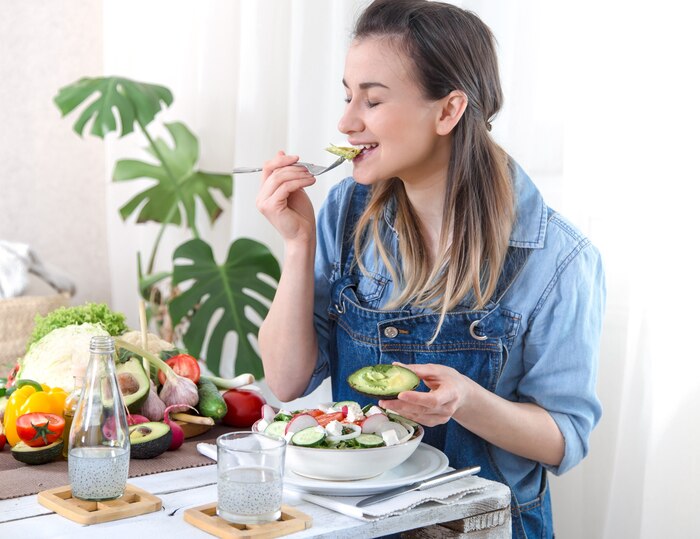 Young and happy woman eating salad at the table