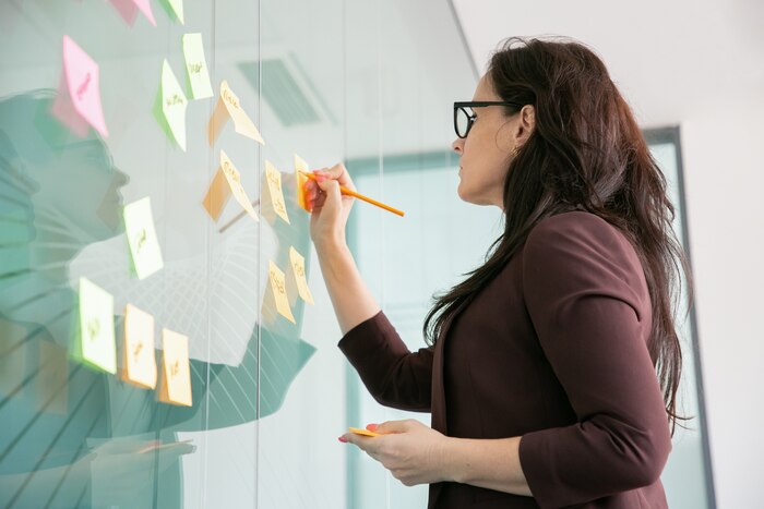 Confident middle-aged businesswoman writing on sticker with pencil and brainstorming