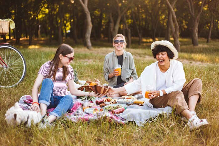 Group of laughing girls happily spending time on beautiful picnic with little dog in park